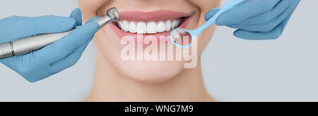 Cropped perfect smile and dentist hands holding a dental drill and an angle mirror. Dentistry and teeth treatment Stock Photo
