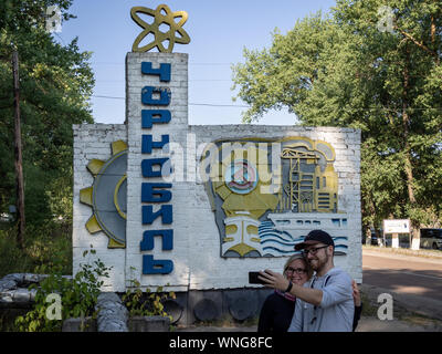 CHERNOBYL, UKRAINE-AUGUST 20, 2019: Couple of young tourists making selfie at the Chernobyl city welcome sign Stock Photo
