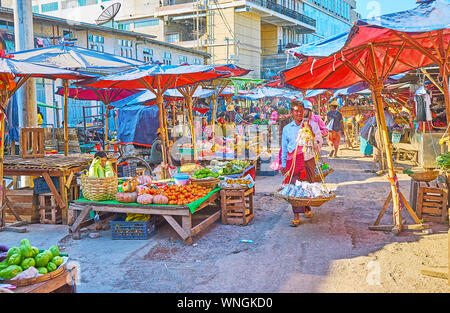 TAUNGGYI, MYANMAR - FEBRUARY 20, 2018: The stalls, offering fresh meat, vegetables and fruits of local farmers are hidden under the large sunshades of Stock Photo