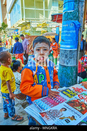 TAUNGGYI, MYANMAR - FEBRUARY 20, 2018: The little Burmese boy with thanaka on face, standing at the newspaper stall in farmers market, on February 20 Stock Photo