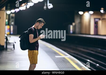 Young man looking at smart phone and waiting on underground station platform. Stock Photo