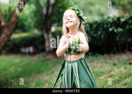 Cute little blonde girl in carnival costume made of green grass outdoor. Stylish kid ready for halloween party Stock Photo