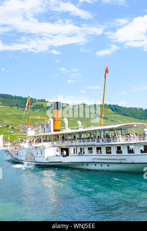 Cully, Switzerland - August 11, 2019: Sightseeing boat with tourists on Lake Geneva. Vineyards on the slopes in background. Lavaux wine region. Tourist boat, cruise. Tourism. Swiss summer. Stock Photo