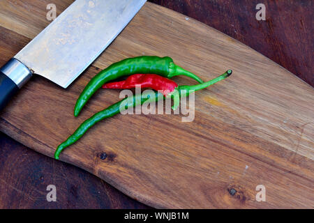 Three hot chilli peppers on wooden chopping board with knife Stock Photo