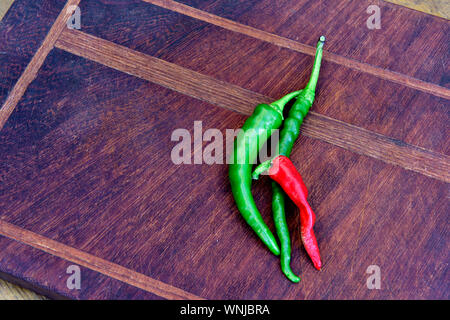 Three hot chilli peppers on wooden chopping board Stock Photo