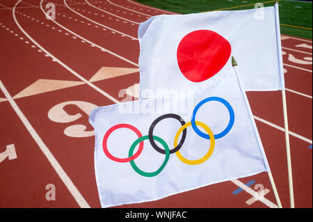 MIAMI, USA - AUGUST, 2019: An Olympic and Japanese flag flutter together above a red athletics track. Stock Photo