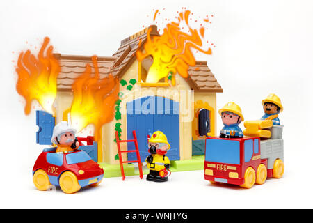 Toy firefighters tackling a toy house that is is on fire, with flames coming out of the windows, shot on a white background Stock Photo