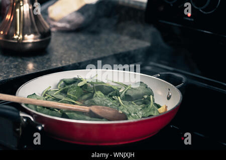 Breakfast in the village. Cooking spinach with scrambled eggs in red pan. Stock Photo
