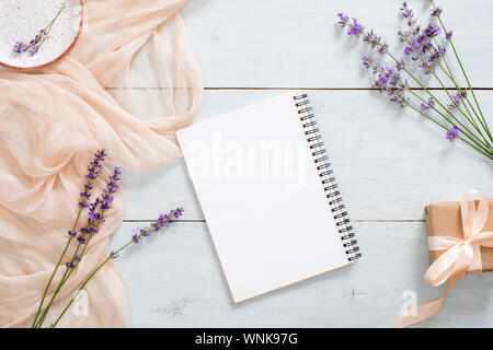 Blank paper notepad, pastel pink color blanket, lavender flowers and gift box on rustic blue wooden background. Top view, tender minimal flat lay styl Stock Photo