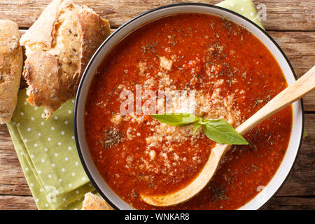 Serving of tomato-basil cream soup with cheese closeup in a bowl and bread on the table. Horizontal top view from above Stock Photo