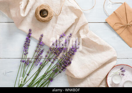 Flatlay lavender flowers, pastel beige blanket, twine, candles on rustic blue wooden background. Feminine desk. Flat lay, top view, overhead. Summer f Stock Photo