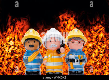 A line of 3 toy firefighters standing to attention, with flames burning in the background Stock Photo