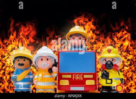 A line of 3 toy firefighters standing to attention, and a fire engine, with flames burning in the background Stock Photo