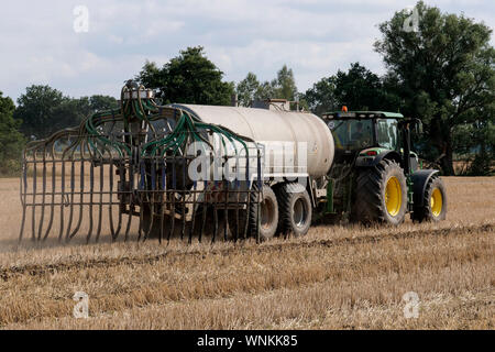 GERMANY, farming, large John Deere tractor with slurry tanker wagon on field, spraying liquid manure as fertilizer on harvested field, slurry from pig and cow sheds with to high nitrate content pollutes groundwater / DEUTSCHLAND, Mecklenburg Vorpommern, Traktor mit Guellewagen bringt Guelle auf ein Stoppelfeld aus, zu viele Nitrate belasten das Grundwasser Stock Photo