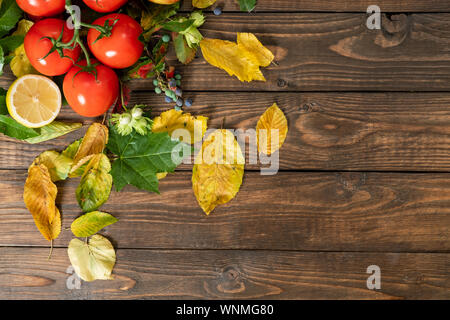 Flatlay autumn composition. Tomato, lemon, autumn fallen leaves on wooden desk. Flat lay, top view, copy space. Agriculture assortment, autumn harvest Stock Photo