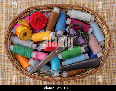 Multicolored sewing threads in a wicker basket. Spools of thread for sewing. The concept of sewing accessories. Stock Photo