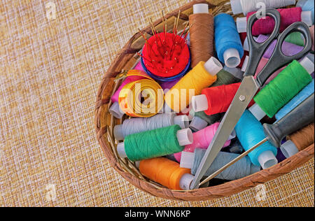 Multicolored sewing threads in a wicker basket. Spools of thread for sewing. The concept of sewing accessories. Stock Photo