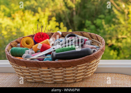 Multicolored sewing threads in a wicker basket. Spools of thread for sewing. The concept of sewing accessories. Stock Photo