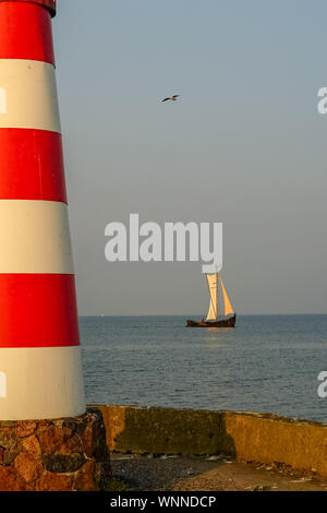 View from the marina with the part of lighthouse on the left in late summer. Sailboat in the cozy golden light of the evening. A bird flies in the sky Stock Photo