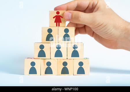 human resources manager is selecting a female worker atop a pyramid made out of male employee icons Stock Photo