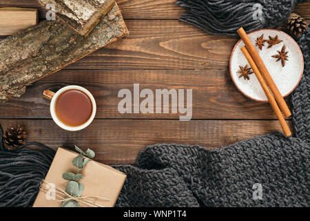 Flatlay hygge style composition with fashion women knitted scarf, mug of tea, gift box, firewood, cinnamon sticks on wooden background. Flat lay, top Stock Photo