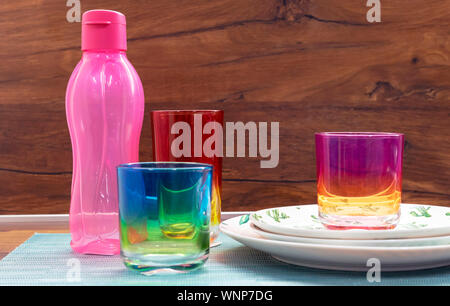 Glasses from multi-colored glass and a pink bottle for cold drinks. Stock Photo