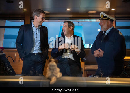 06 September 2019, Bavaria, Weßling: Markus Söder (M), Prime Minister of Bavaria, is standing on the bridge of the Seeshaupt during the navigation on the Starnberger See within the framework of the CSU board meeting on the bridge of the Seeshaupt next to Markus Blume (l), Secretary General of the CSU, and Günter Engel-Art, Captain of the Seeshaupt. The CSU executive board holds a two-day retreat. At the end of the meeting at Lake Starnberg, the new 'climate strategy' is to be adopted, with which the CSU intends to enter the decisive phase of coalition discussions on a major climate protection Stock Photo