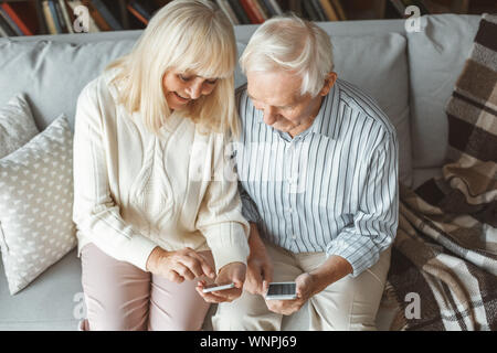 Senior couple together at home retirement concept sitting browsing smartphone showing Stock Photo