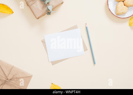 Autumn composition. Cozy feminine desktop with letter, blank paper card, gift box, cookies, fallen leaves on pastel beige background. Flat lay, top vi Stock Photo