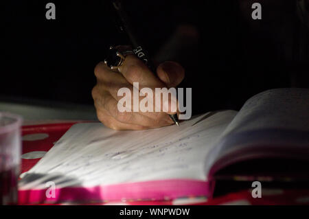 Older man or woman's hand with a large gemstone ring writing into a notebook Stock Photo