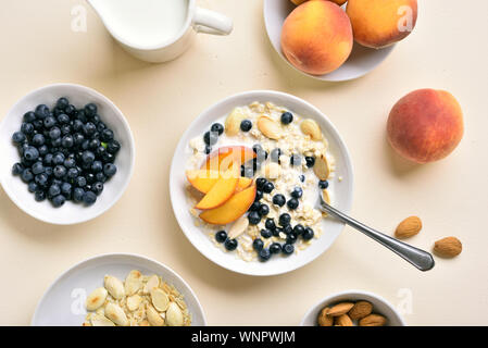 Tasty diet oatmeal porridge with peach slices, almond and wild blueberries in bowl over light stone background. Healthy food concept. Top view, flat l Stock Photo