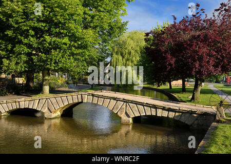 Bridge over the River Windrush in morning sun with trees in Bourton-on-the-Water village in the Cotswolds England Stock Photo