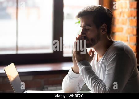 Worried man thinking about problem puts hands together in prayer Stock Photo