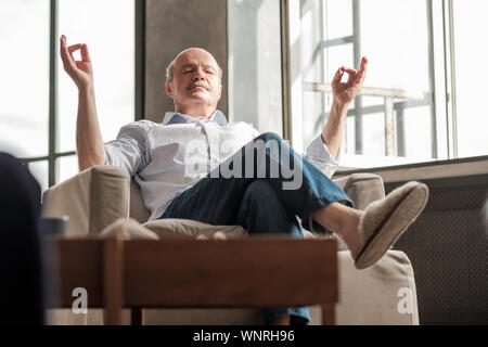 Senior hispanic man meditating on the sofa in the living room. stay calm during everyday troubles. Stock Photo