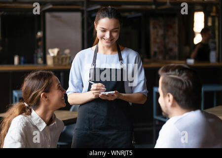 Young couple ordering food in cafe, smiling waitress serving customers Stock Photo