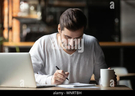 Focused man using laptop and writing notes in coffeehouse Stock Photo