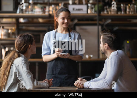 Couple making order in cafe, smiling waitress writing in notepad Stock Photo