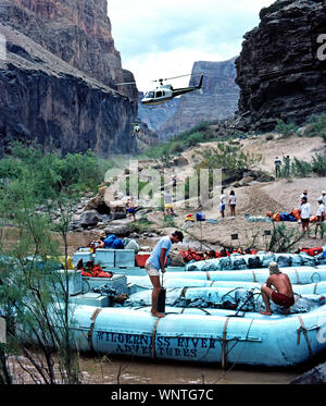 Helicopters descend between canyon walls with adventure travelers who join other passengers waiting to board two large neoprene rafts for a float trip down the Colorado River that runs through Grand Canyon National Park in Arizona, USA. Each of the outboard motor-powered boats carries up to 14 passengers and two crew members, plus food and camping supplies for 3-1/2 to 8-day outings that wind from 88 to 188 miles (142 to 303 kilometers) through the famous river canyon. The longer the trip, the more thrills through water-splashing rapids along the way; life jackets are provided. Transportation Stock Photo
