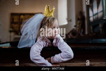 girl sat with a dress up crown & veil on her head, looking thoughtful Stock Photo