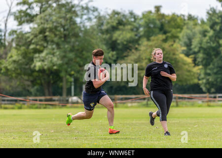 Amateur touch rugby player (man, age 20) running with rugby ball in hands, with both feet off the ground, and female teammate prepares to receive pass Stock Photo