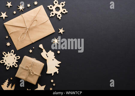 Christmas wooden decorations, gift box, kraft paper envelope with letter on dark black background. Christmas greeting card mockup. Minimal flat lay st Stock Photo