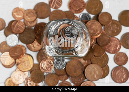 Full jar of coins from above, surrounded by loose change. Money saving and investment concept Stock Photo