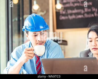Businessman who is engineer seriously look at laptop of coworker and hold a cup of coffee in the meeting at office in the morning Stock Photo