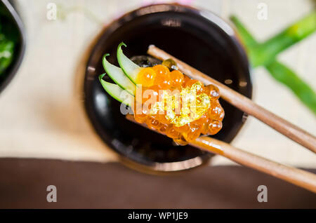 Wooden chopsticks tongs Gunkan Maki Sushi with salmon caviar (Ikura) and cucumber in Japanese food restaurant. Stock Photo