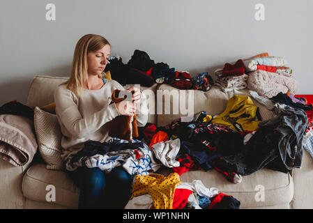 Woman folding large pile of laundry on sofa at home Stock Photo