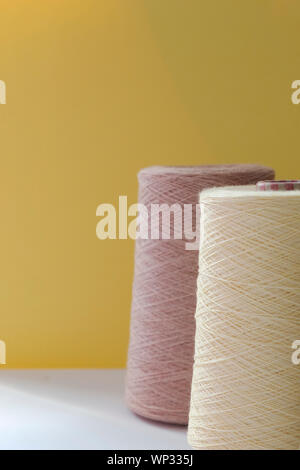 Pastel color bobbins of wool yarn for hand and machine knitting on a yellow background. Stock Photo