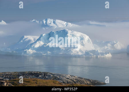 Stranded icebergs in the fog at the mouth of the Icefjord near Ilulissat. Nature and landscapes of Greenland. Travel on the vessel among ices. Stock Photo