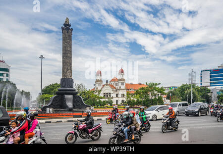 busy traffic at Tugu moda stone monument commerorating Indonesian Independance against the backdrop of the former colonial-era headquarters of the Dut Stock Photo