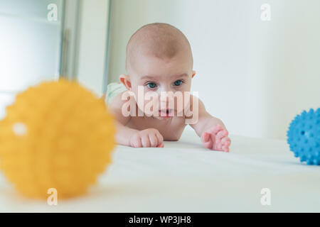 A small child crawls on the changing table and playing a rubber ball. Stock Photo