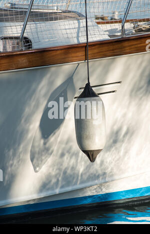 Single white fender hanging on the hull of a sailboat casting a double shadow in the sunlight in a transport, boating and sport concept Stock Photo